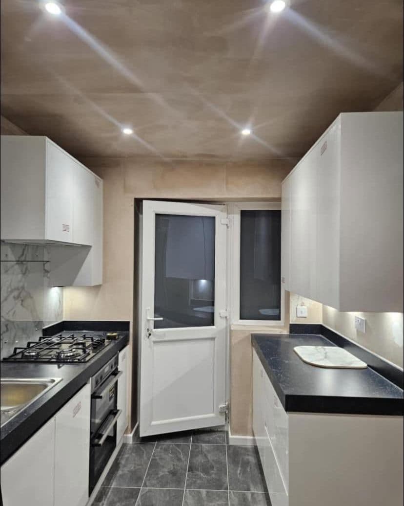 Galley kitchen with white units, black worktops and downlights