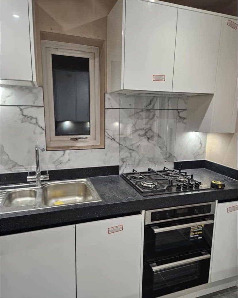 Fitted white gloss kitchen with a marble-effect splashback and black worktops